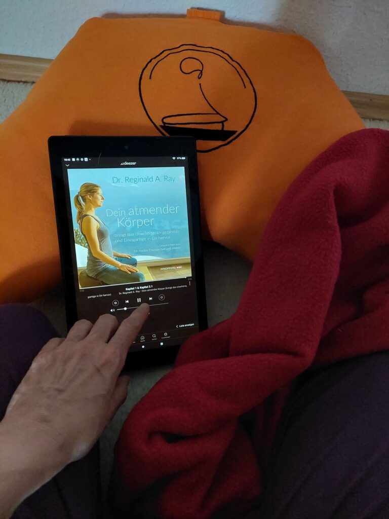 Ein IPad liegt auf einem Mediationskissen. Eine Hand bedient den Bildschirm.