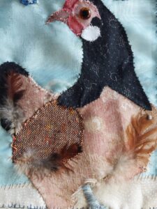 Ausschnitt einer textilen Hühnercollage mit Knopfauge, echten Federn und applizierten Stoffen.