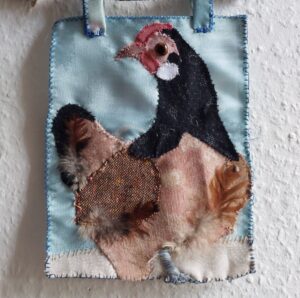 extile Wandcollage eines Huhns aus verschiedenen Stoffen, Knopfauge und echten Federn.