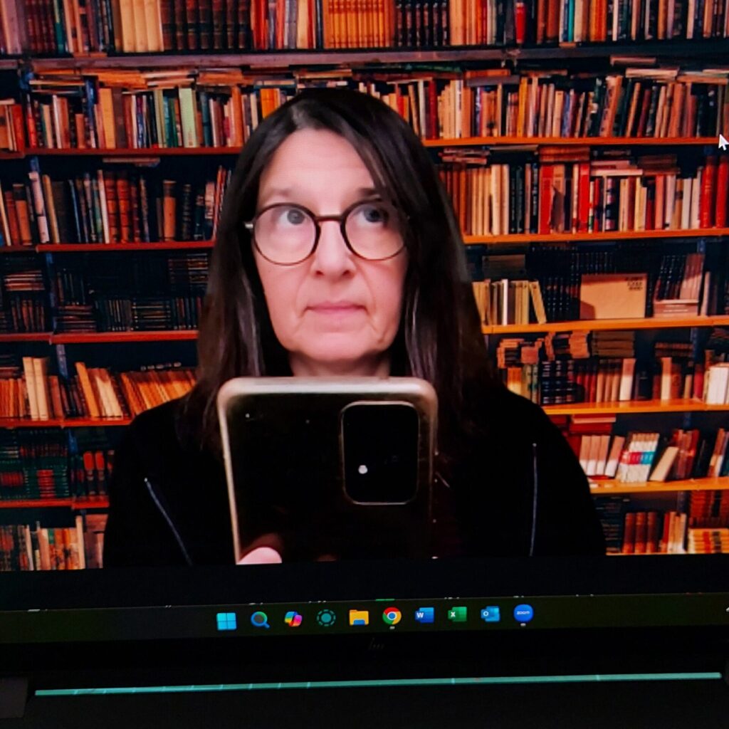 Selfie vom Bildschirm vor einem Zoom-Termin, mit virtueller Bücherwand im Hintergrund