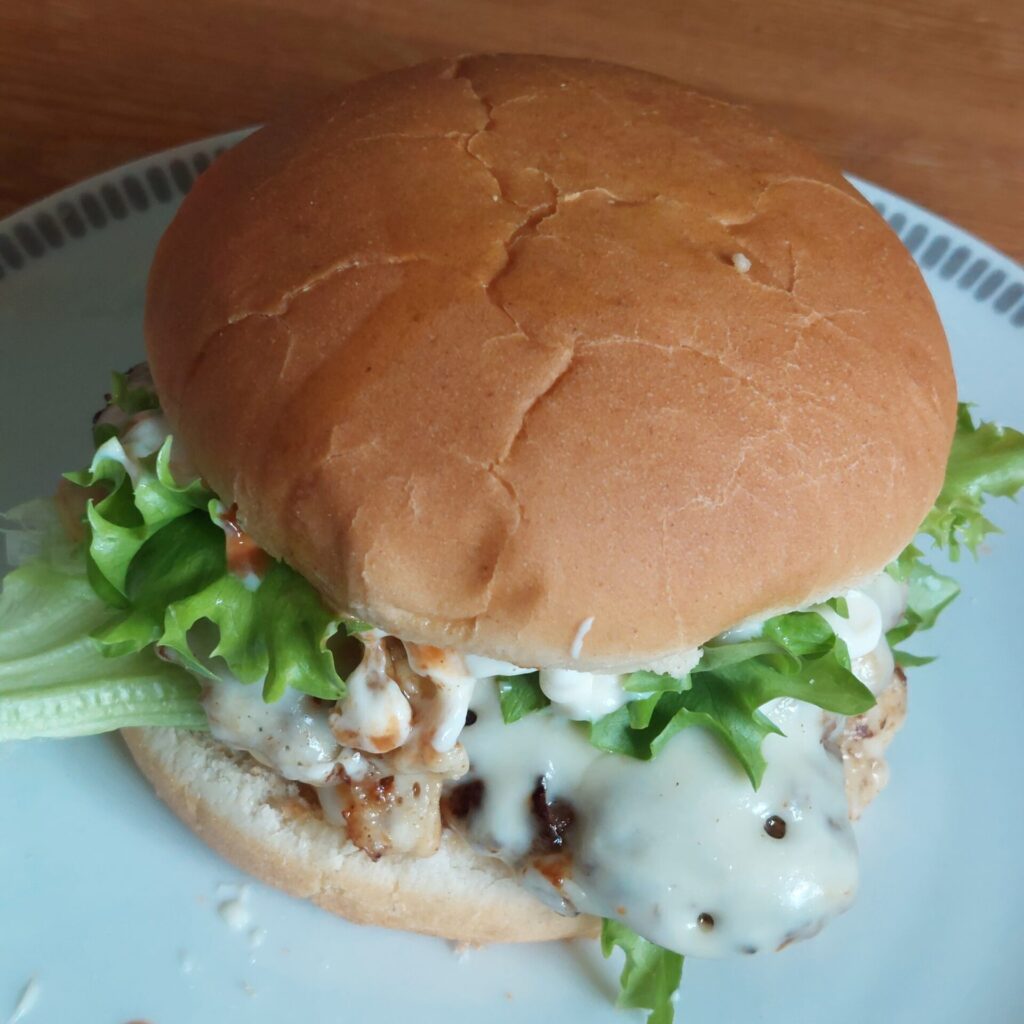 Selbstgemachter Hamburger mit Salat und Soße auf einem Teller als Mittagessen.