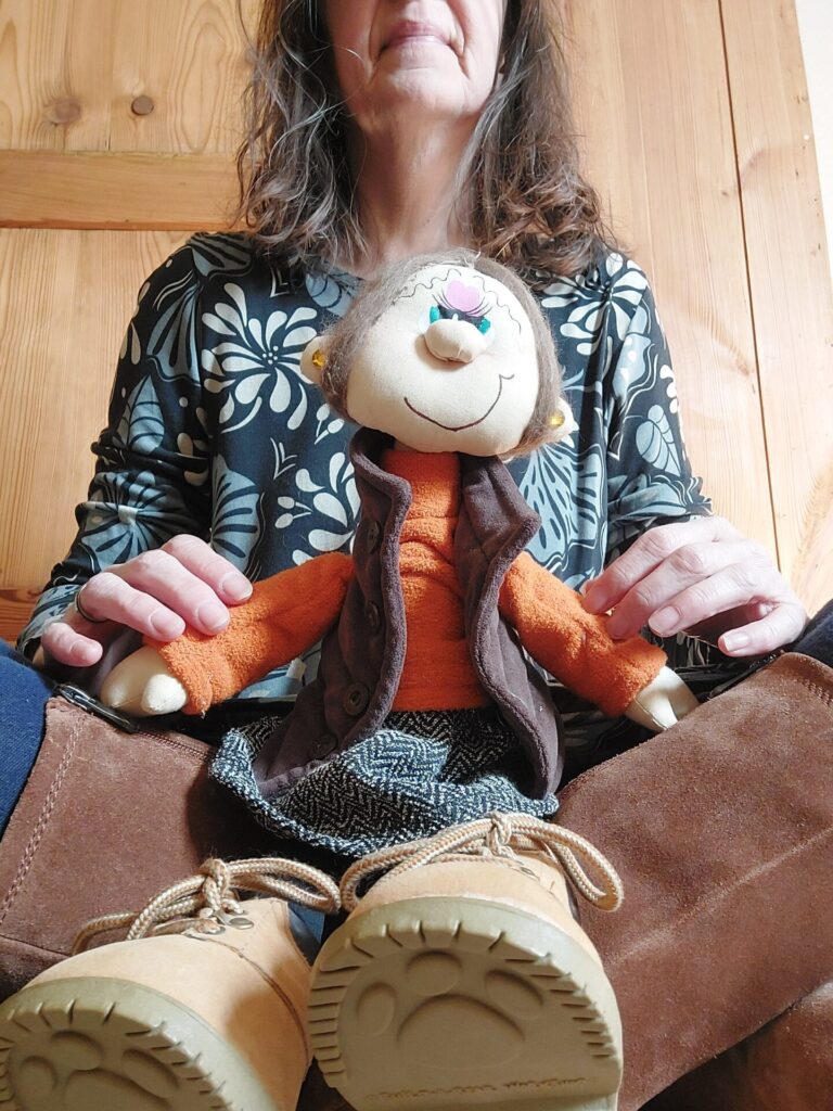 Frau sitzt mit einer Puppe auf dem Schoß und hält sie mit beiden Händen – inneres Kind als Teil von Selbstbeziehung.