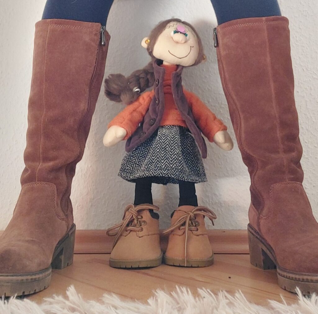 Puppe steht zwischen den Stiefeln einer Frau – inneres Kind zwischen Schutz und Begrenzung.