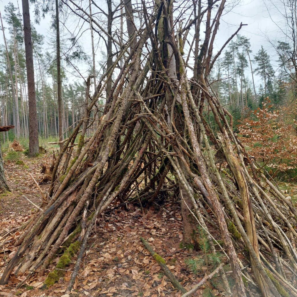 Selbstgebautes Tipi aus Ästen im Wald, gewachsenes Spiel- und Bauprojekt während der Osterferien.