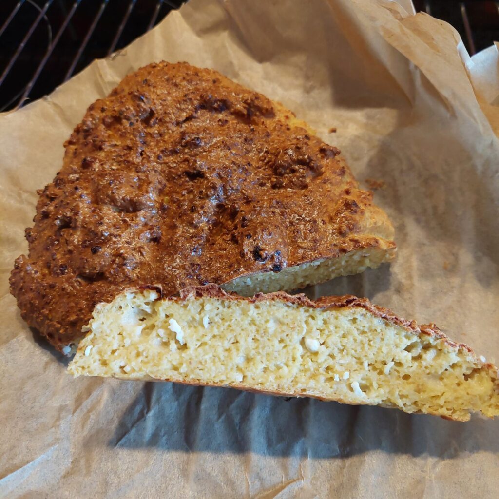Angeschnittenes frisch gebackenes Brot mit goldbrauner Kruste liegt auf Backpapier.
