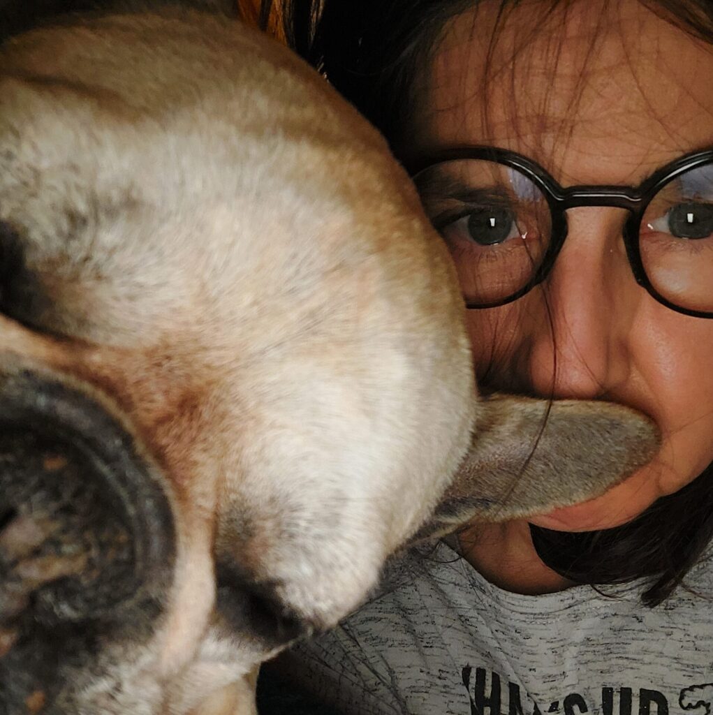 Nahaufnahme eines Selfies mit Hundeschnauze und Hundeohr vor dem Gesicht einer Frau mit Brille.