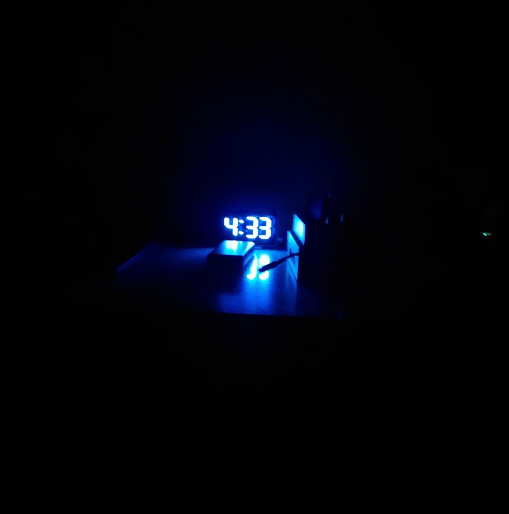 Dunkles Zimmer mit leuchtender digitaler Uhr, die 4:33 Uhr anzeigt.