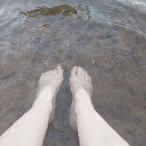 Zwei nackte Füße stehen im klaren, flachen Flusswasser.