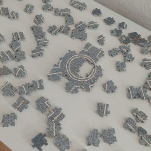 Graue Puzzleteile liegen sortiert auf einem weißen Tisch, erste Teile sind zusammengesetzt.