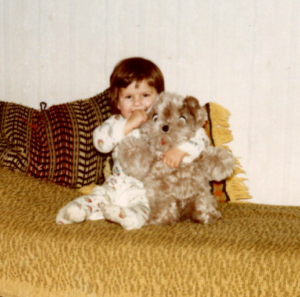 Kleines Kind sitzt mit großem Teddy auf dem Sofa.