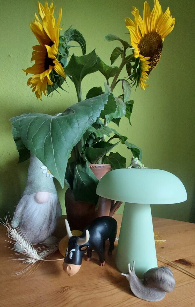 Spätsommerliche Tischdekoration mit grünem Wichtel, Pilz, Frosch, Stier, Schnecke, Kornähren und Sonnenblumen.