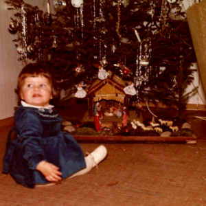 Kleines Kind sitzt vor Weihnachtsbaum und Krippe.