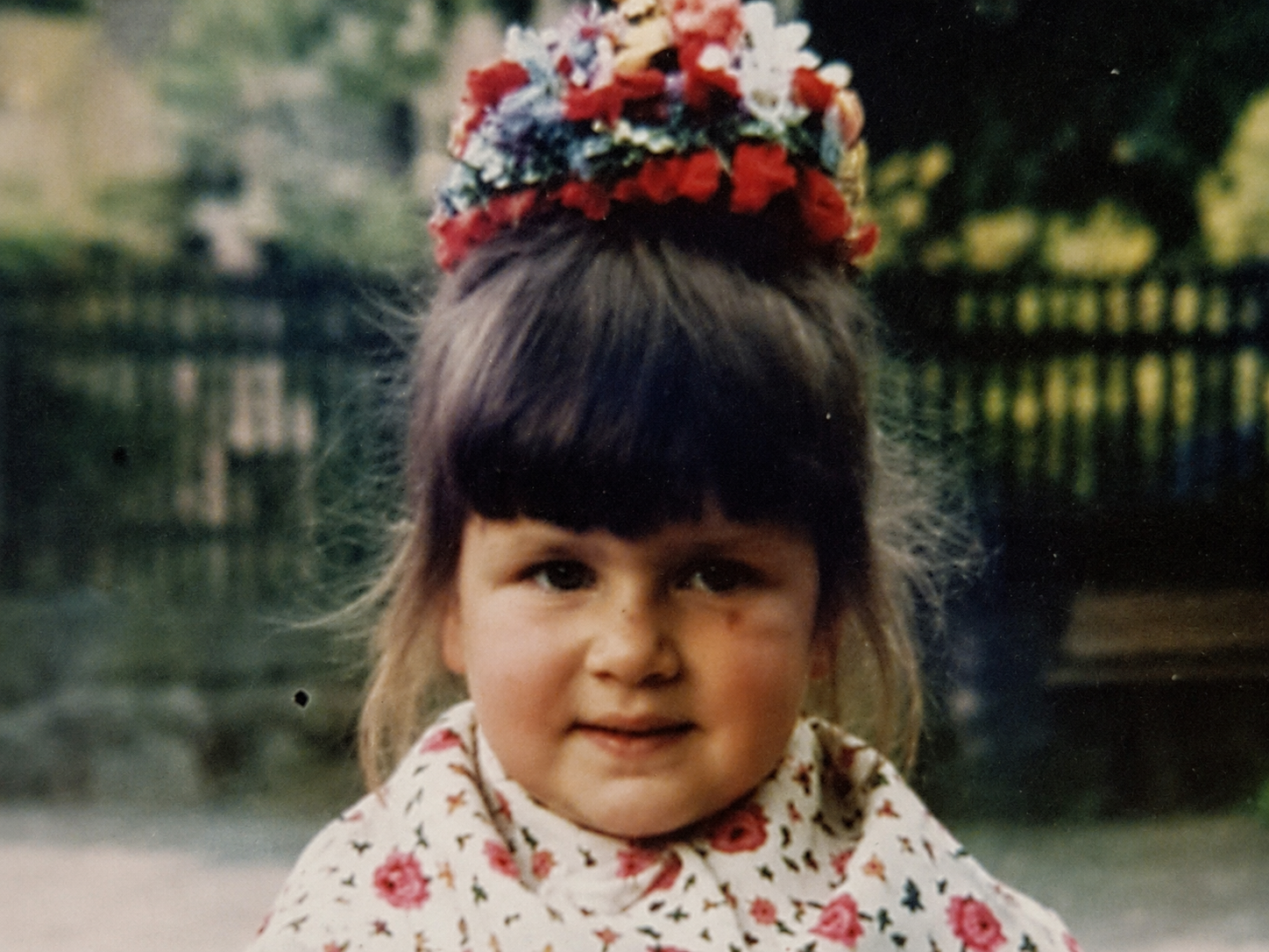 Silke als kleines Mädchen in Hersfelder Tracht mit Schnierhaid und geblümtem Schultertuch, als Nahaufnahme vor unscharfem Hintergrund.