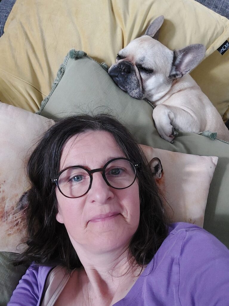 Silke liegt auf dem Sofa, während Hündin Lotte hinter ihrem Kopf zwischen den Kissen schläft.